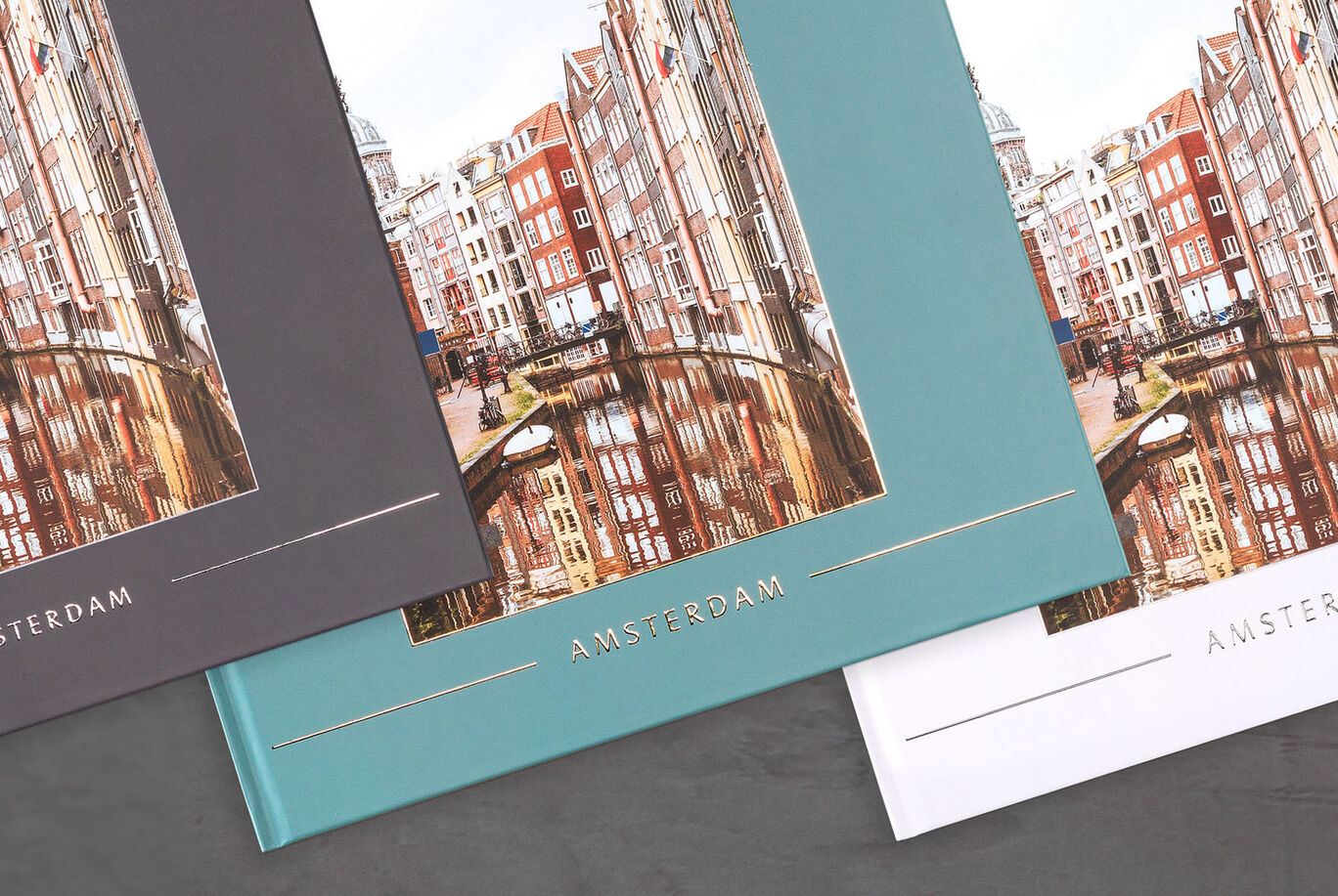 Tre fotobøker med Amsterdam bybilder på en mørk bakgrunn